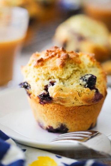 A close-up view of a lemon and blueberry jumbo muffin sitting a small white plate with a fork next to it.