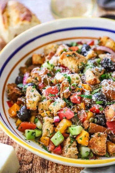 A straight-on view of a large serving pasta bowl filled with panzanella that has been topped with shaved Parmesan cheese.