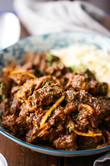 A close-up view of Thai beef with red curry sauce in an Asian bowl with Jasmine rice on the side.