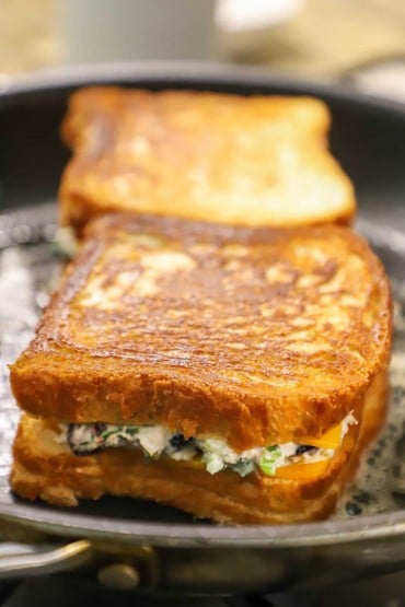 A close-up view of two tuna melt sandwiches in a skillet being browned in bubbling melted butter.