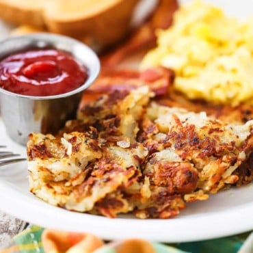 A close-up view of crispy diner-style hash brown on a plate next to a small metal container of ketchup.