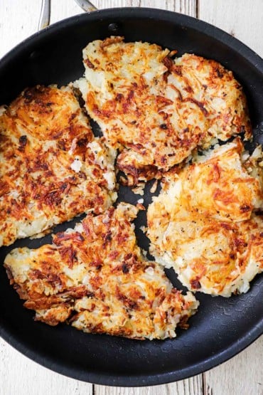An overhead view of a large non-stick skillet filled with diner-style crispy hash browns.