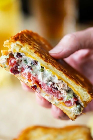 A close-up view of a person holding up a tuna melt sandwich that has been sliced in half.