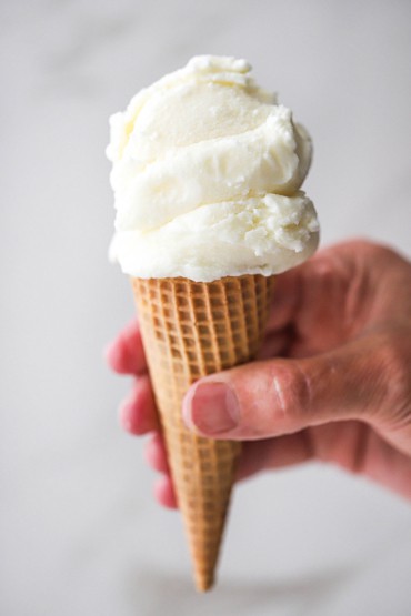 A person holding a sugar ice cream cone with two scoops of homemade vanilla ice cream on top.