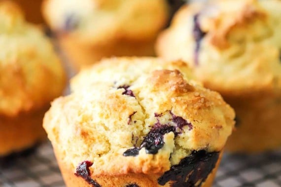 A straight-on view of a lemon blueberry jumbo muffin sitting on a baking rack with other muffins in the background.
