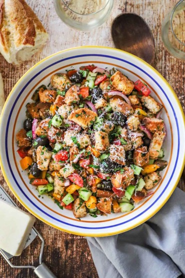 An overhead view of a large pasta bowl filled with panzanella and flanked by a block of Parmesan cheese and a torn loaf of bread.