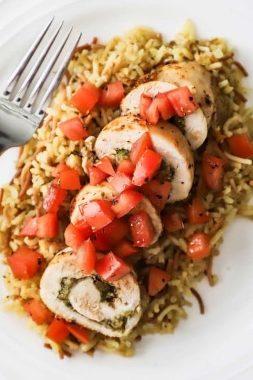 A close-up view of plate filled with sliced pesto-stuffed chicken with tomato relish all on a bed of rice pilaf.