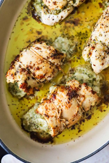 An overhead view of four chicken breasts that have been rolled up stuffed with pesto and baked in a dish.