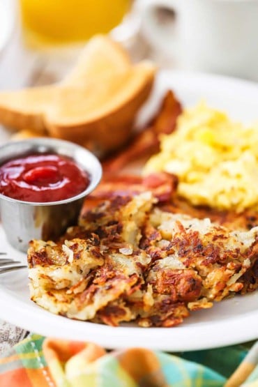 A close-up view of crispy diner-style hash brown on a plate next to a small metal container of ketchup.