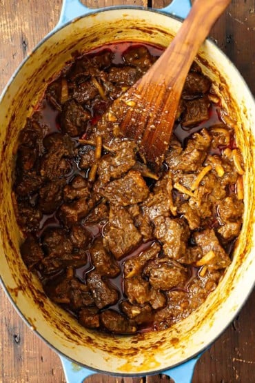 An overhead view of slow-cooked pieces of beef in a Thai red curry sauce in an oval Dutch oven.