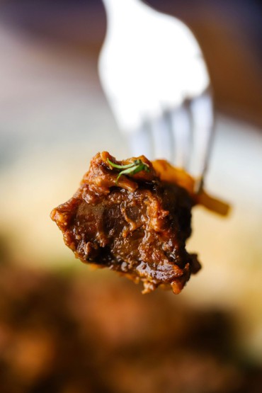 A fork that is being used to hold up a piece of Thai beef that has been slow-cooked in a red curry and coconut sauce.