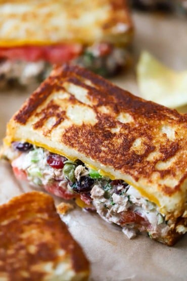 A view of several tuna melt sandwiches that have been cut in half. Capers and dried cranberries are visible along with the tuna.