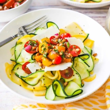 A straight-on view of a bowl filled with a zucchini and yellow squash salad with tomato relish and fresh Parmesan shavings.