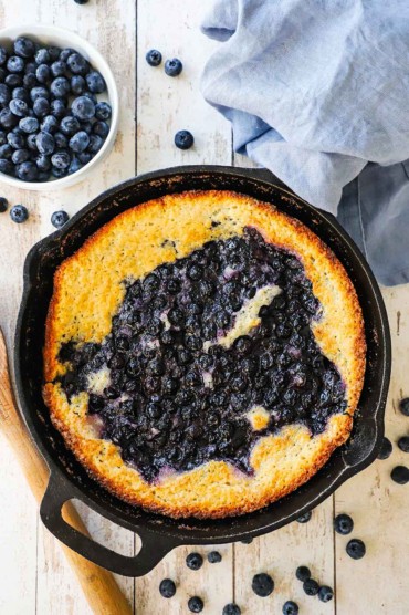 An overhead view of a black cast-iron skillet that is full of an untouched blueberry cobbler with crusty lightly browned edges.