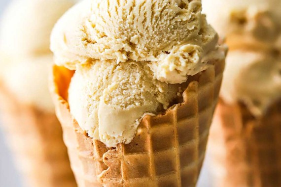 A waffle cone with two scoops of salted caramel ice cream that has been inserted into a metal holder with two other cones in the background.
