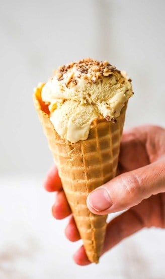 A person holding a waffle ice cream cone that is filled with salted caramel ice cream that has been topped with toffee bits.