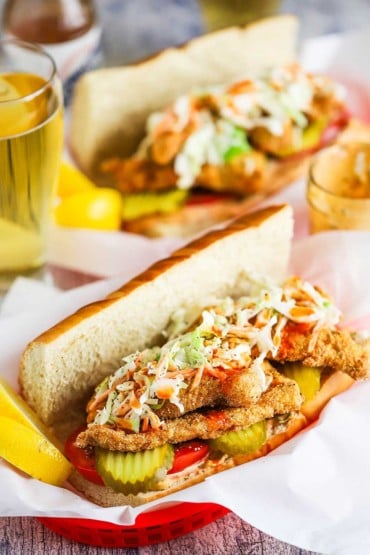 A straight-on view of two baskets filled with a fried catfish po-boy sitting next to a tall glass of beer.