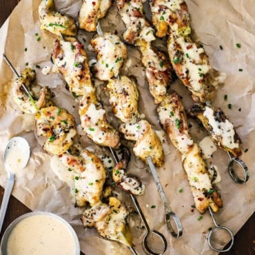 An overhead view of grilled chicken skewers with Alabama sauce on a piece of crumpled brown wax paper.