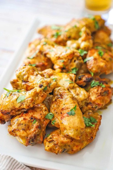 A straight-on view of a pile of grilled curry chicken wings on a white rectangular platter.