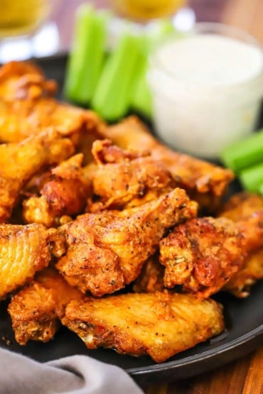 A close-up view of classic Buffalo wings on a black plater with a jar of blue cheese dressing in the background.