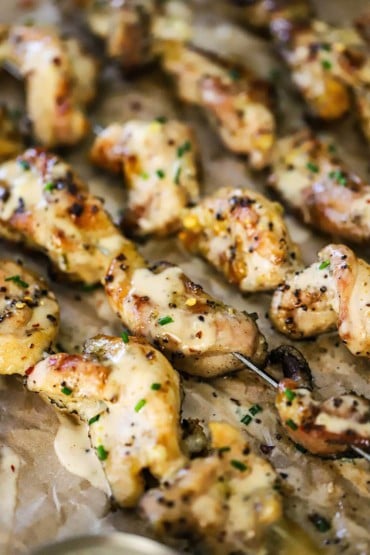 A close-up view of a grilled chicken skewers that have a layer of Alabama white sauce drizzled over the top.