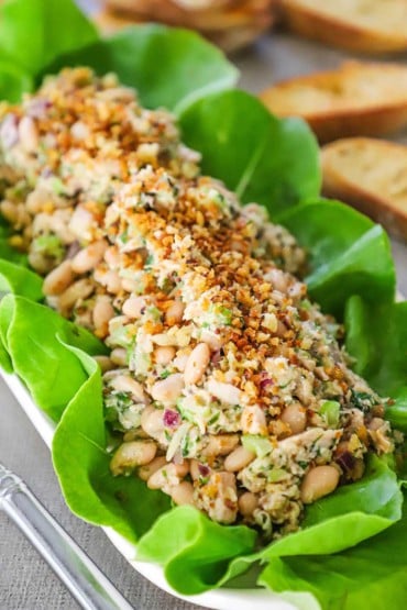 A straight-on view of a albacore tuna and white bean salad on a bed of green leaf lettuce on a rectangular serving platter.