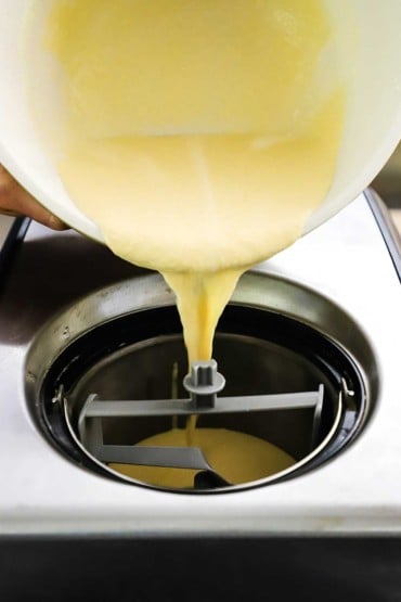 A creamy custard being poured from a large ceramic bowl into the canister that is resting in an electric ice cream maker.