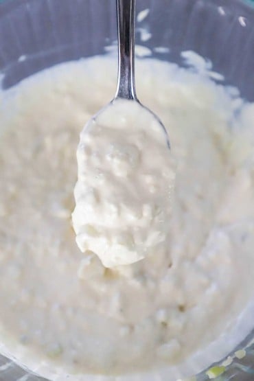 An overhead view of a spoon of gorgonzola dipping sauce being lifted from a glass bowl filled with the sauce.