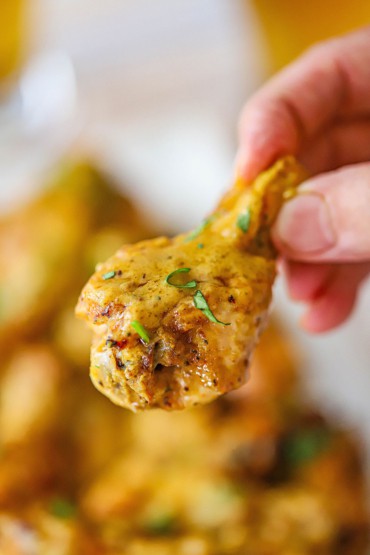 A person holding a grilled curry chicken wings with a few pieces of chopped cilantro stuck to the wing.