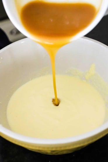 Homemade caramel sauce being poured from a small white bowl into a ceramic bowl filled with an ice cream custard.