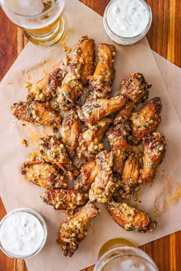 An overhead view of a serving of garlic Parmesan wings on two pieces of brown paper with two small jars of blue cheese dressing nearby.