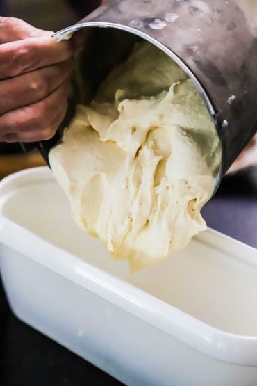 Soft ice cream being transferred from an ice cream canister into a rectangular plastic ice cream container.