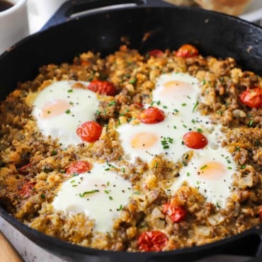 A straight-on view of a skillet breakfast in a large cast-iron skillet filled with a breakfast sausage hash topped with cooked eggs.