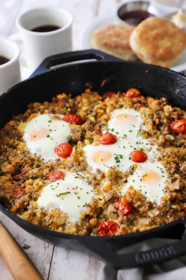 A straight-on view of a skillet breakfast in a large cast-iron skillet filled with a breakfast sausage hash topped with cooked eggs.