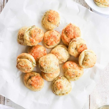 An overhead view of a pile of bacon parmesan gourgeres on a square white wax piece of paper.