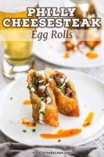 A Philly cheesesteak egg roll that has been cut in half and the two halves are sitting on a white plate upright.