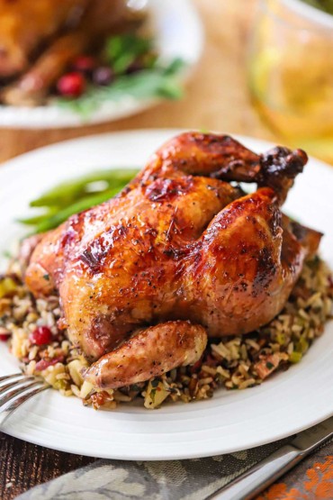 A close-up view of a port-glazed Cornish hen sitting on top of a bed of wild rice pilaf on a white dinner plate.
