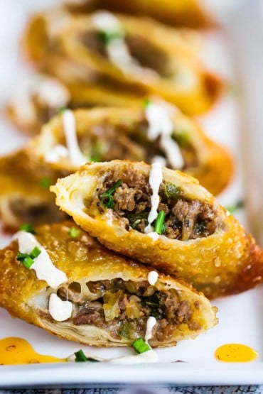 A close-up view of a row of Philly cheesesteak egg rolls that have been split in half and sitting on a white platter.