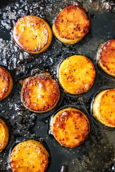 An overhead view of fondant potatoes being seared in a black cast-iron skillet filled with melted duck fat.