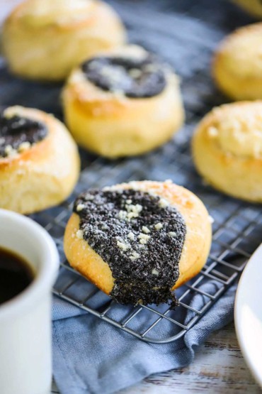 A straight-on view of a poppyseed filled kolache sitting on a baking rack next to more kolaches and a mug of black coffee.