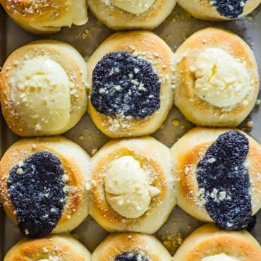 An overhead view of a baking pan filled with freshly baked kolaches topped with poppyseed filling and cream cheese filling.