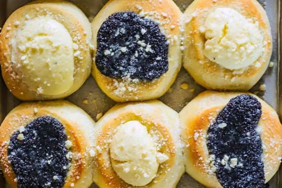 An overhead view of a baking pan filled with freshly baked kolaches topped with poppyseed filling and cream cheese filling.
