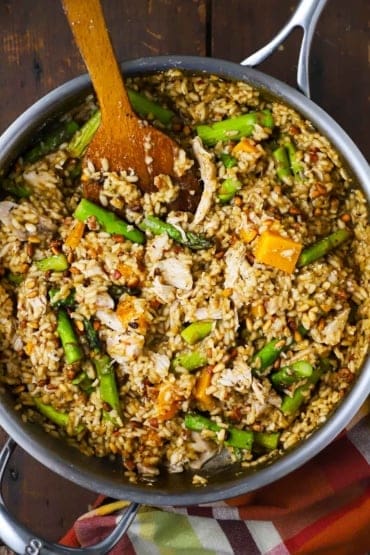 An overhead view of a large silver skillet filled with risotto with left-over turkey, roasted butternut squash, and asparagus.