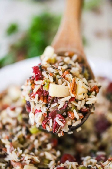 A large wooden spoon holding up a heaping helping of wild rice with pecans and cranberries stuffing.