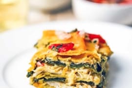 A square slice of a green enchilada casserole with layers of roasted chicken, sauce, roasted peppers, and melted cheddar cheese.