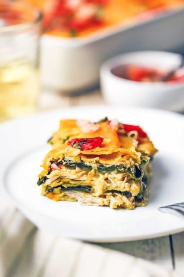 A square slice of a green enchilada casserole with layers of roasted chicken, sauce, roasted peppers, and melted cheddar cheese.