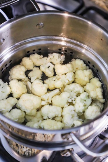 An overhead view of a medium-sized pasta pot filled with cauliflower florets that are being boiled.