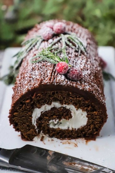 A close-up view of the end of a yule log with the interior circular chocolate sponge cake the envelopes a white filling an is topped with chocolate frosting and powdered sugar.