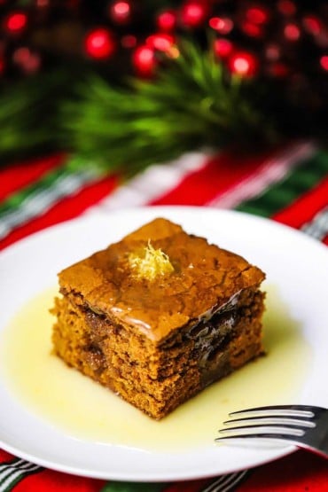 A square slice of gingerbread cake sitting in a small pool of lemon sauce and topped with a small pile of lemon zest.