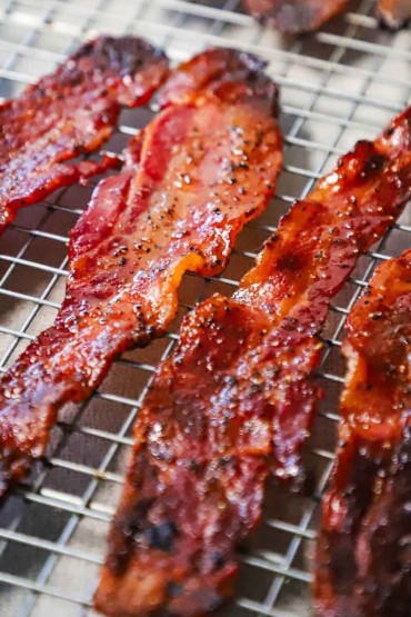 A straight-on view of cooked strips of maple pepper bacon resting on two baking racks.